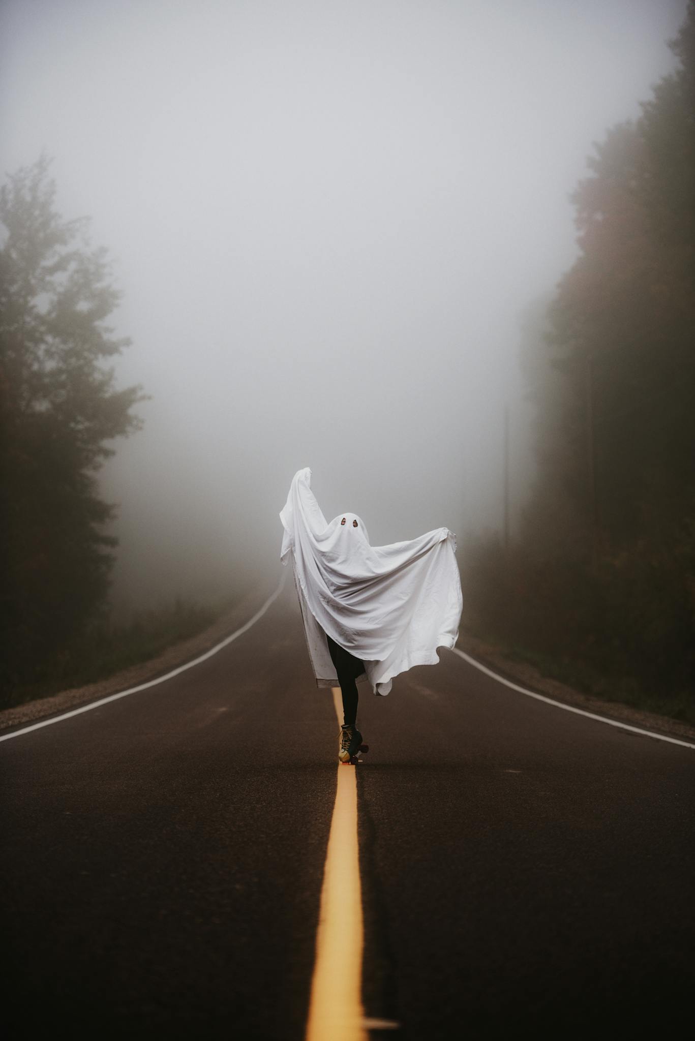 A person dressed as a ghost on a foggy road, embodying the Halloween spirit.